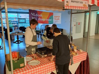 Drie jonge leerlingen staan poffertjes te bakken bij een poffertjeskraam