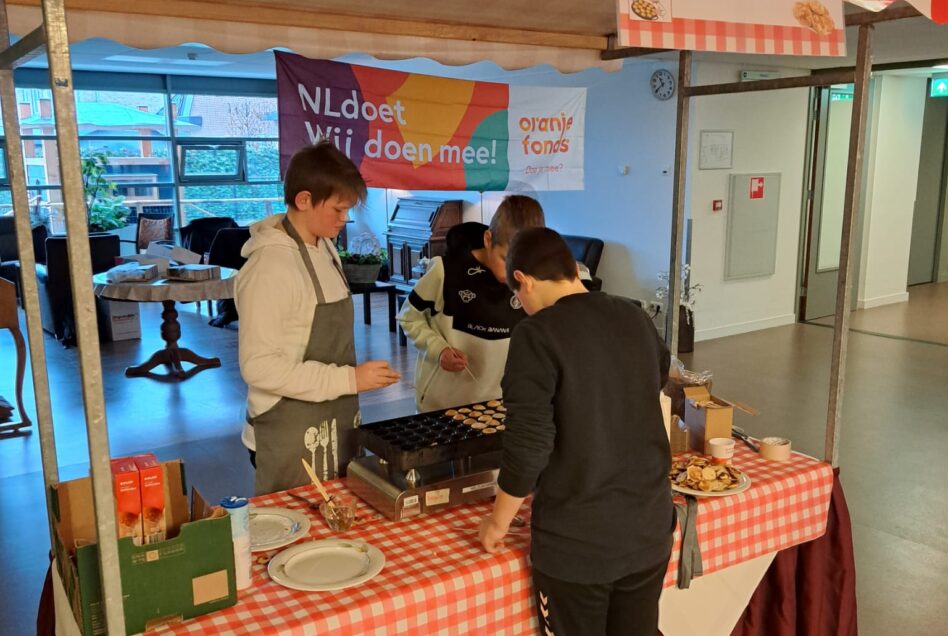 Drie jonge leerlingen staan poffertjes te bakken bij een poffertjeskraam