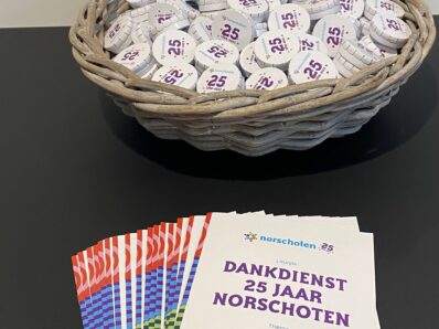 Liturgieën en blikjes pepermuntjes met het jubileumlogo van Norschoten liggen in een mandje.
