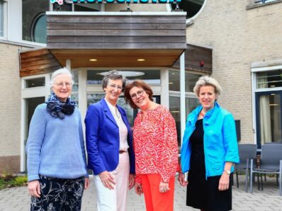 Drie medewerkers van het eerste uur en de huidige directeur staan voor de ingang van zorgorganisatie Norschoten locatie Klaverweide in Barnveld.
