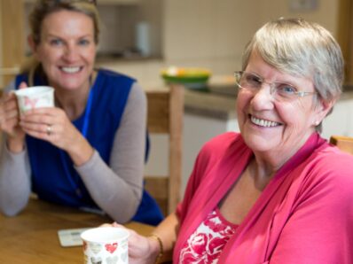 Twee dames hebben een mokje in de handen en lachen.